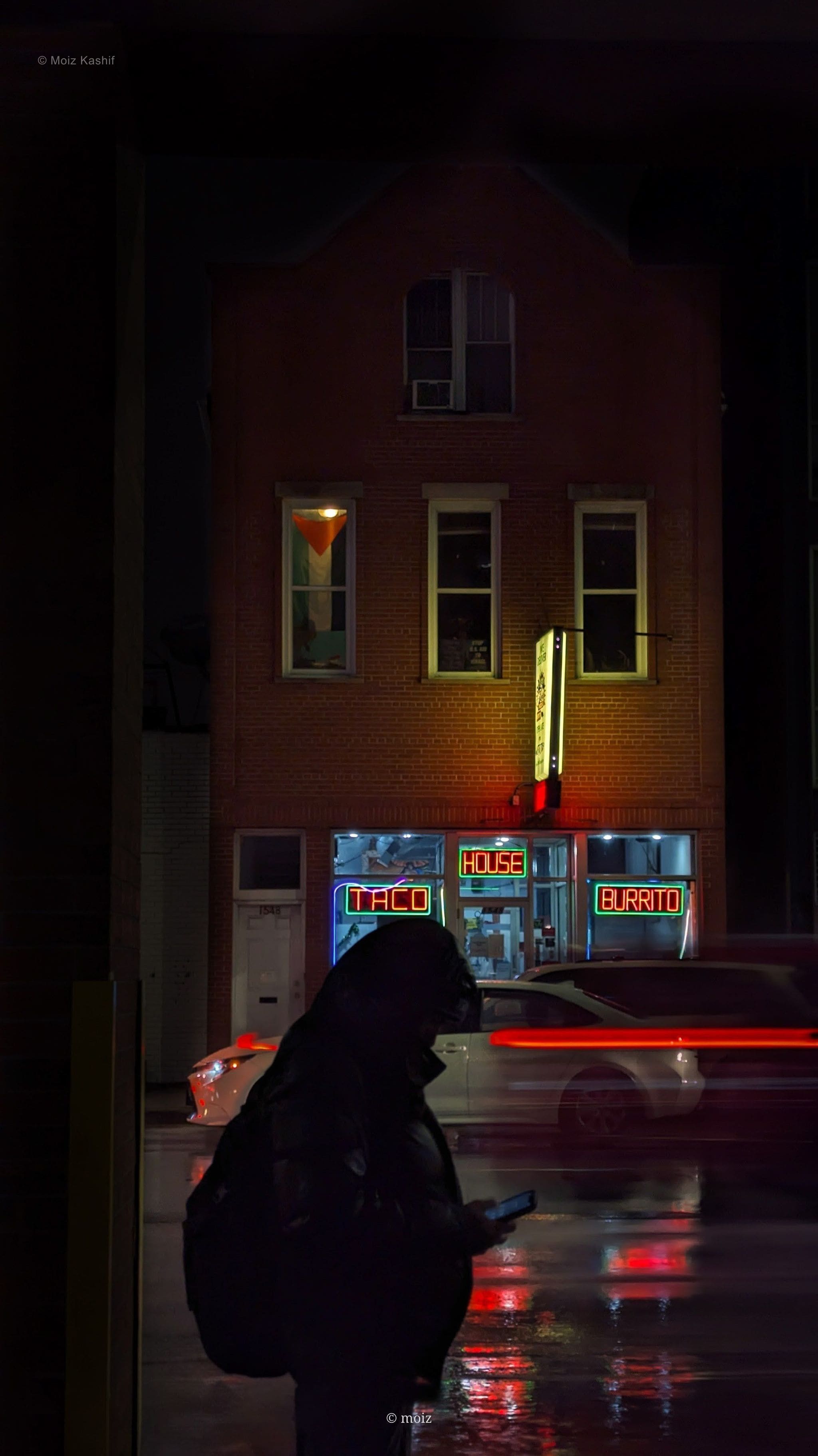 A hooded pedestrian crossing a rain-slick Chicago street at night.