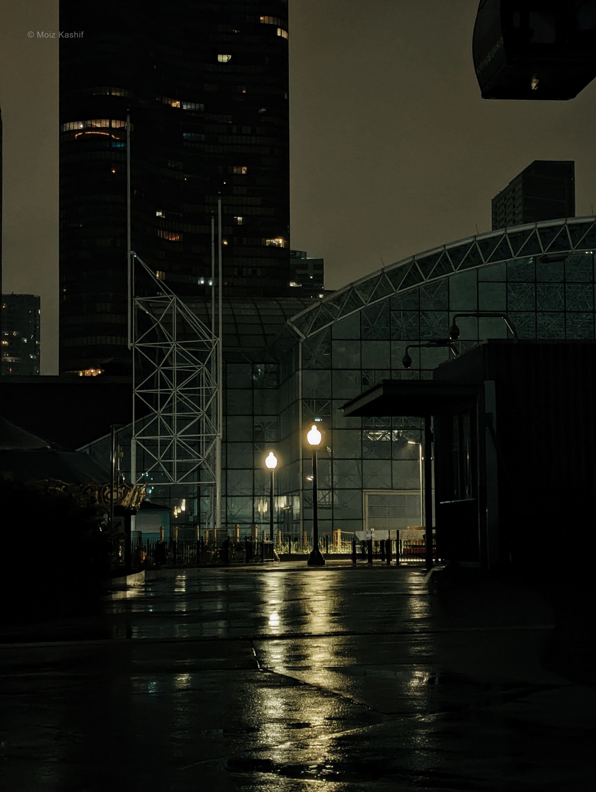 Glass architecture and streetlamps reflected across wet pavement.