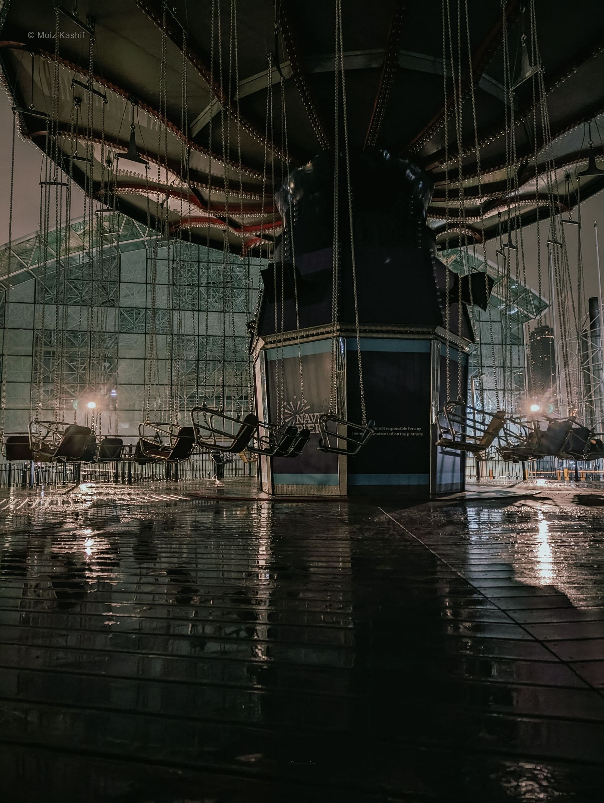 A mirrored glass facade and empty chairs reflected after rain.