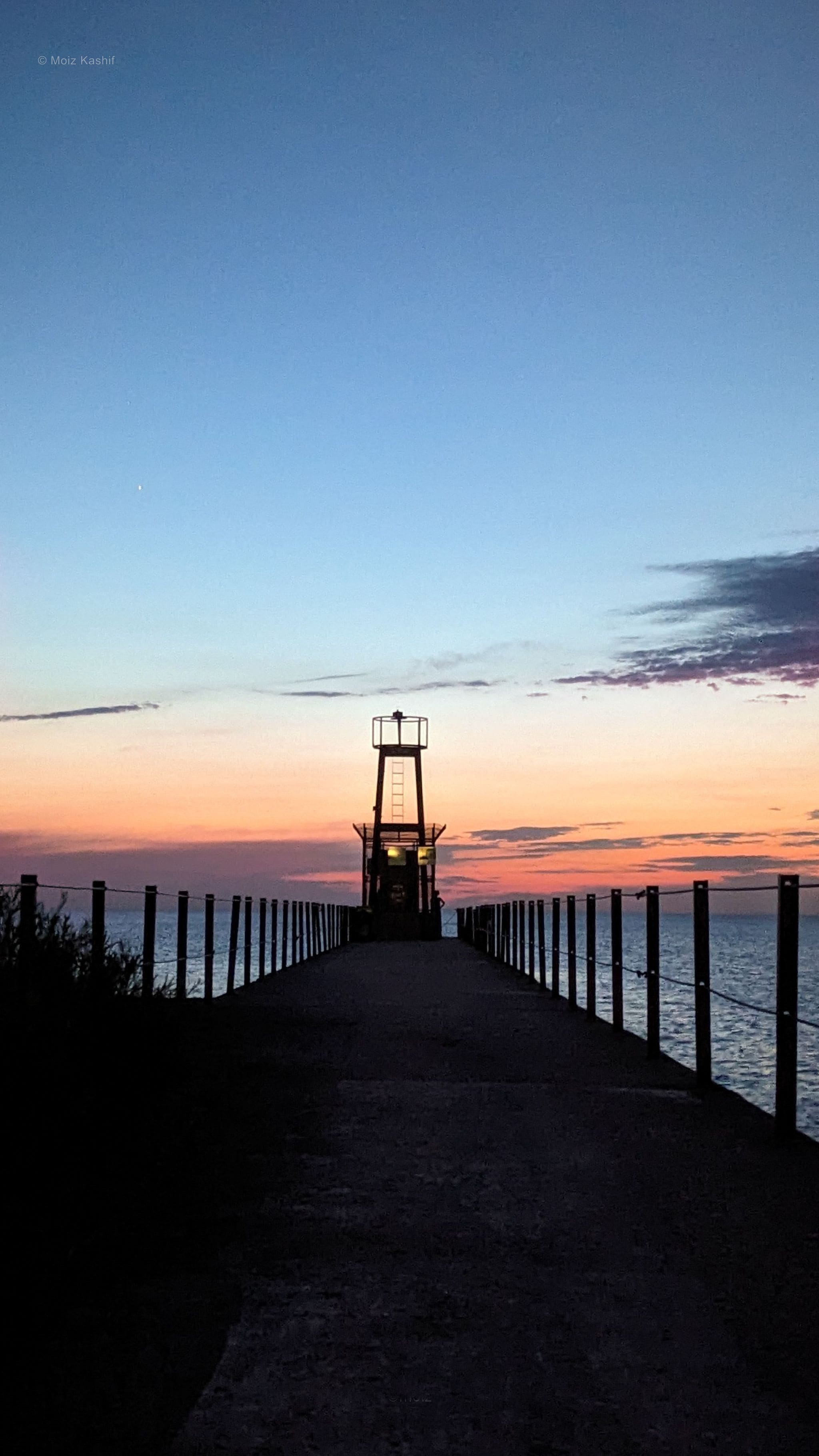 A narrow pier reaching toward the horizon under blue and peach evening light.