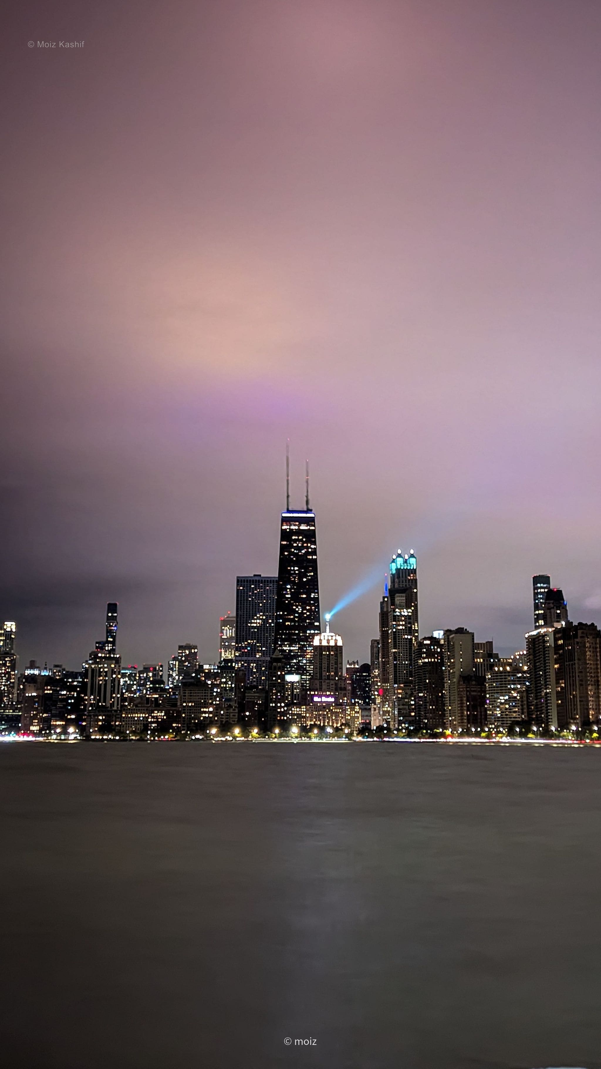 The Chicago skyline glowing across dark water beneath a violet sky.