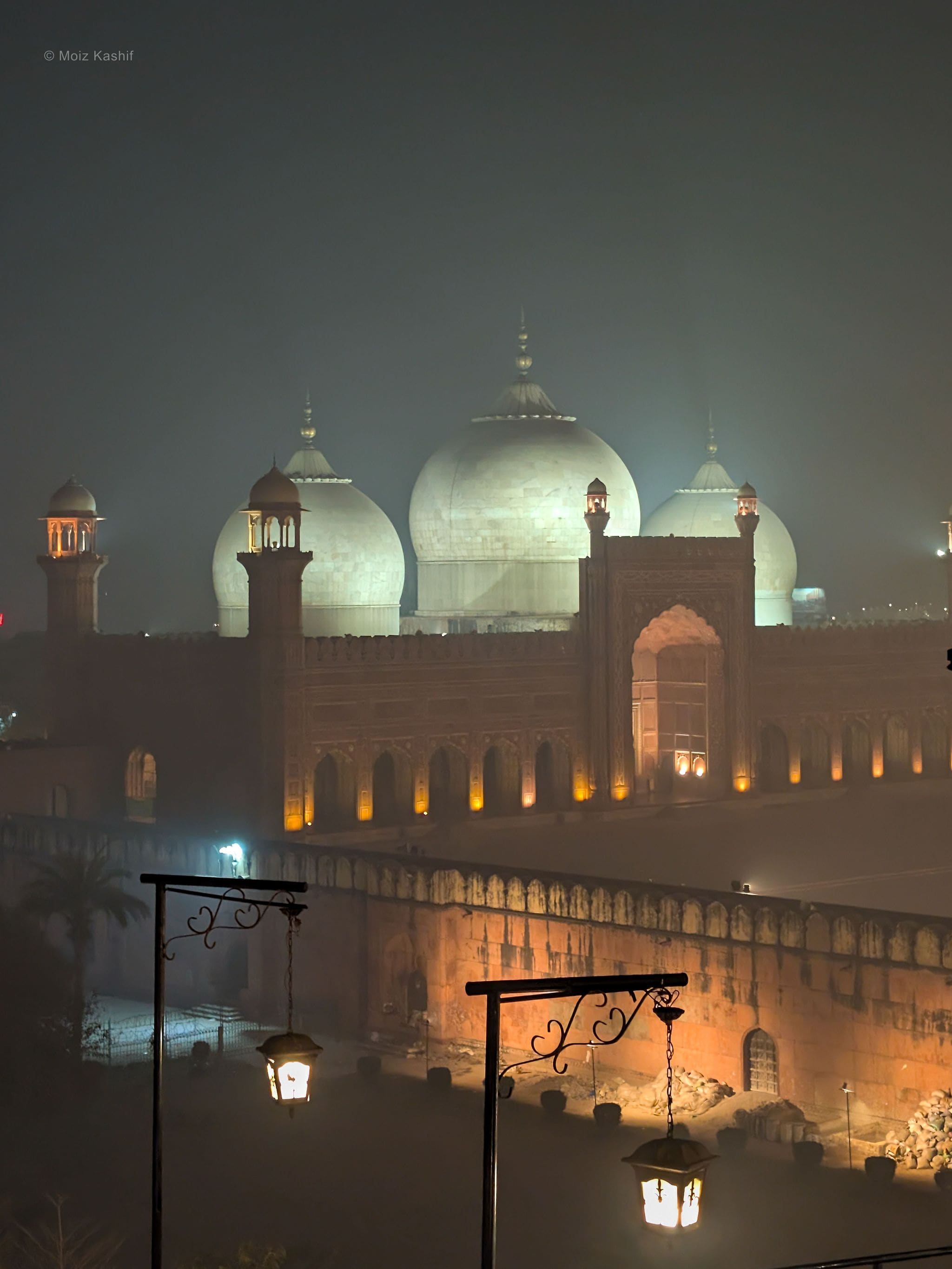 A domed mosque glowing through dense fog above warm streetlamps.