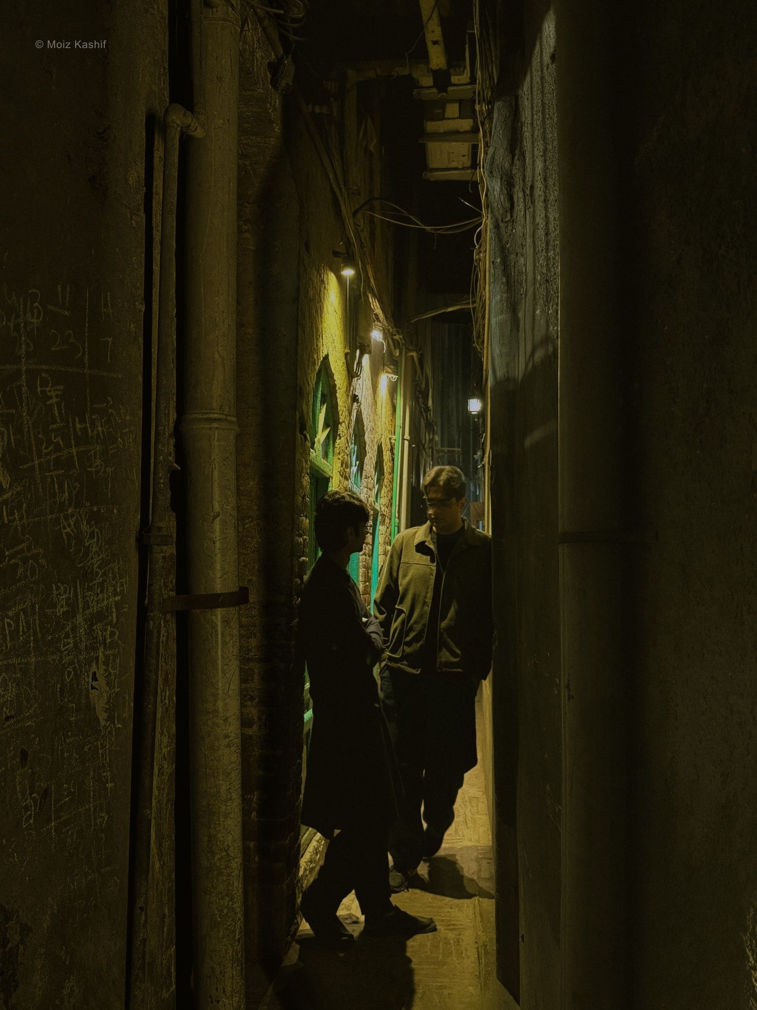 Two figures meeting in a narrow dimly lit alley.