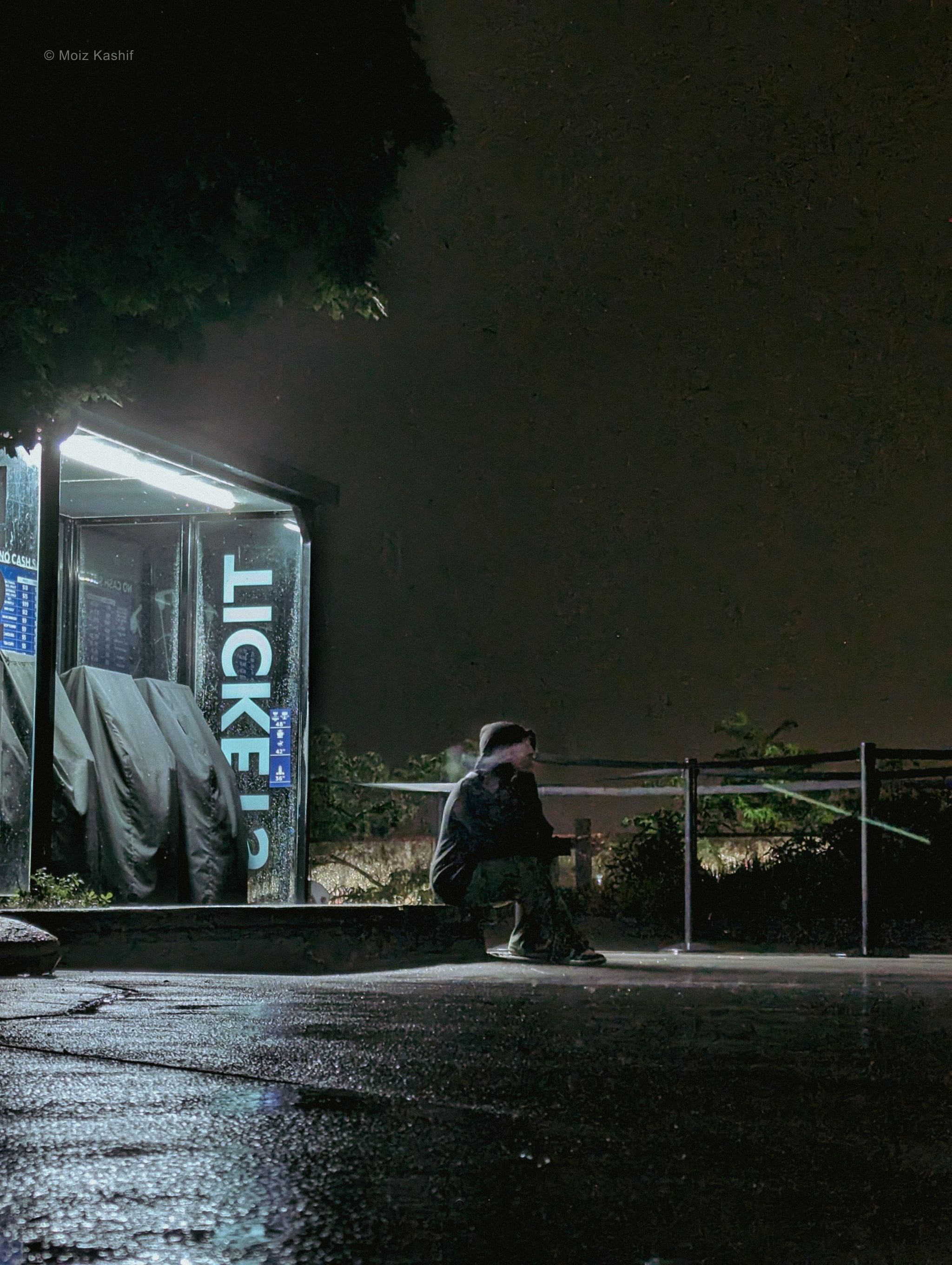 A solitary person resting beside a turquoise ticket booth.