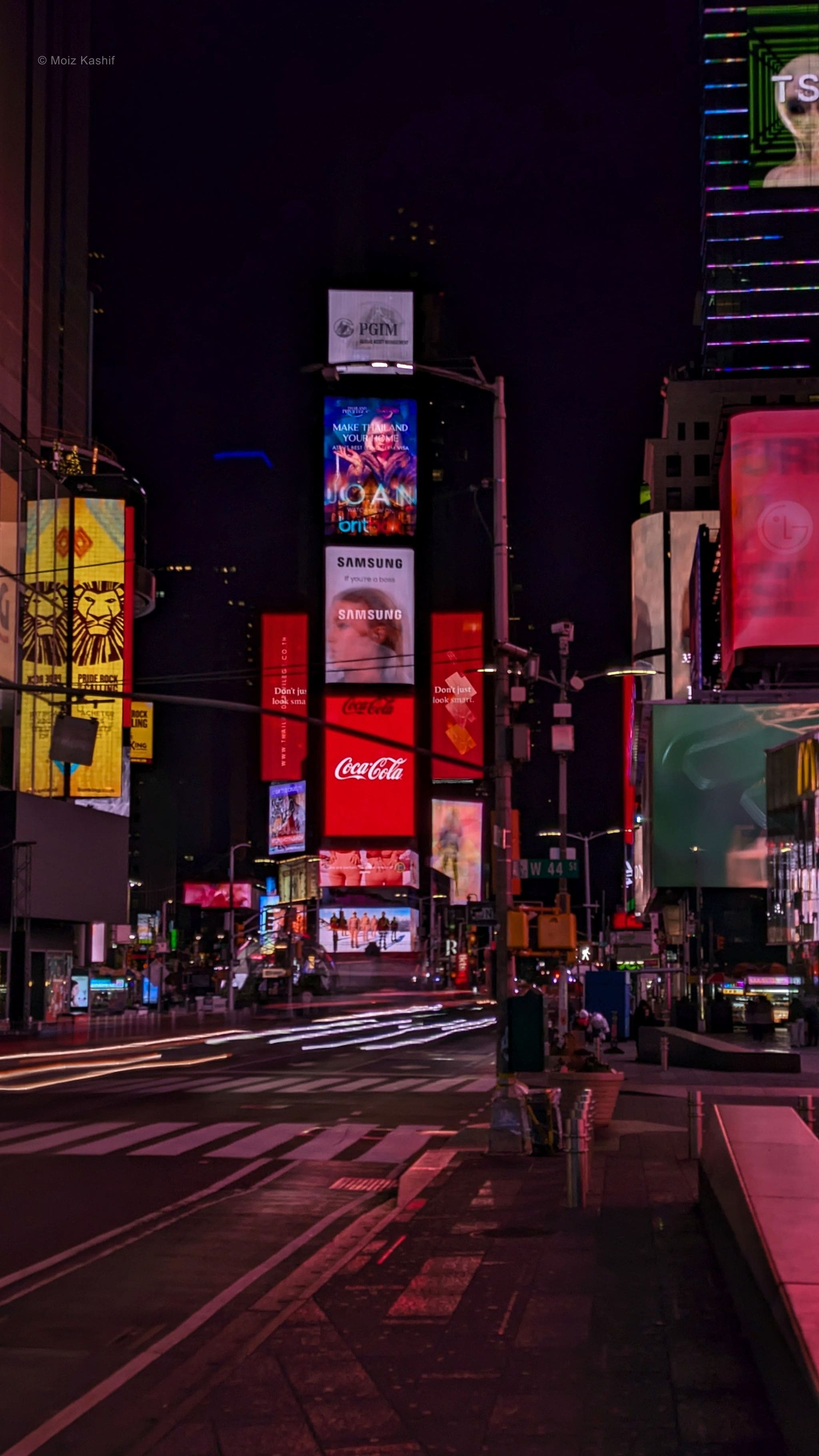 Times Square nearly empty beneath red and violet signs before dawn.