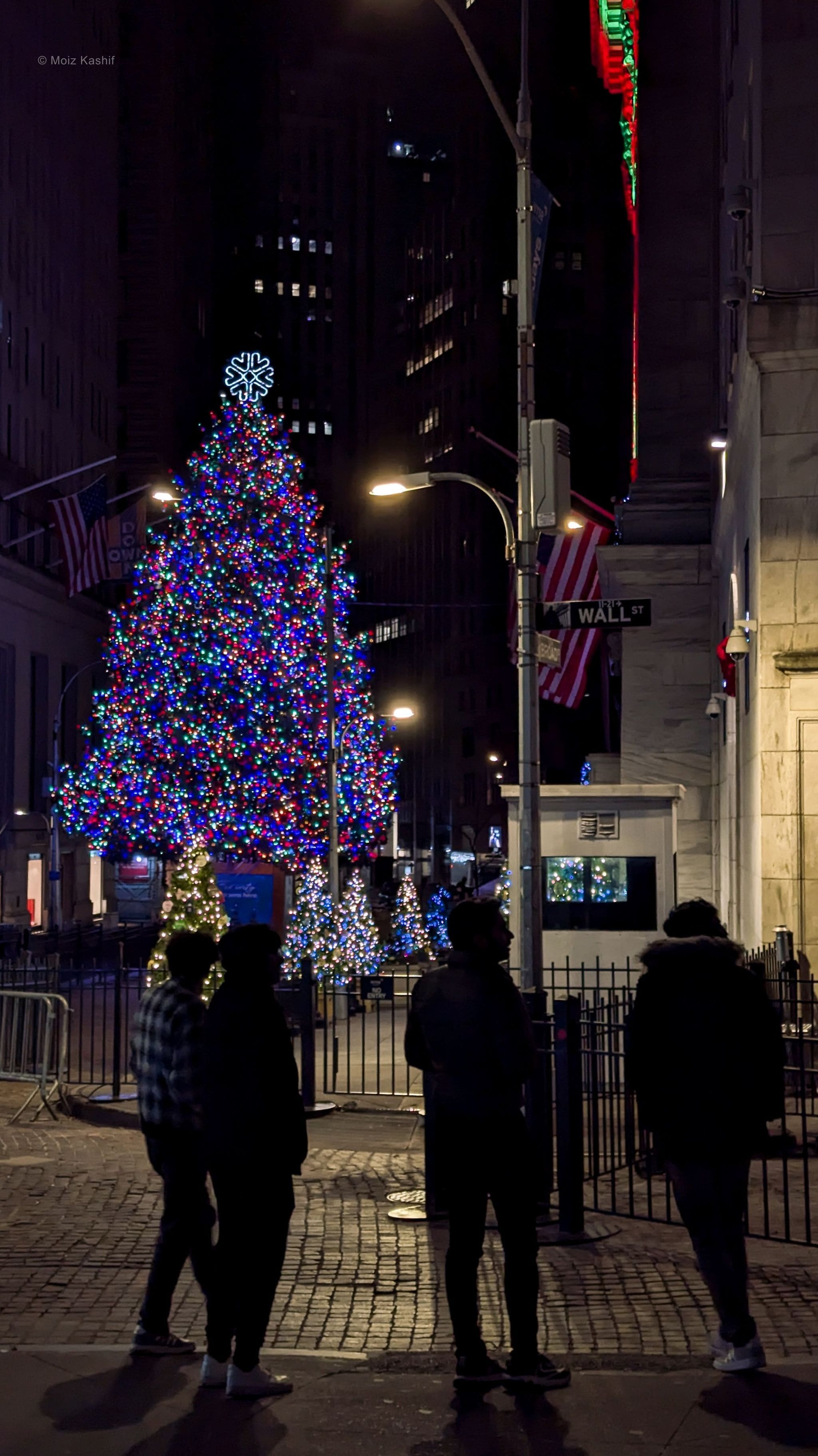 Figures gathered before an illuminated Christmas tree on Wall Street.